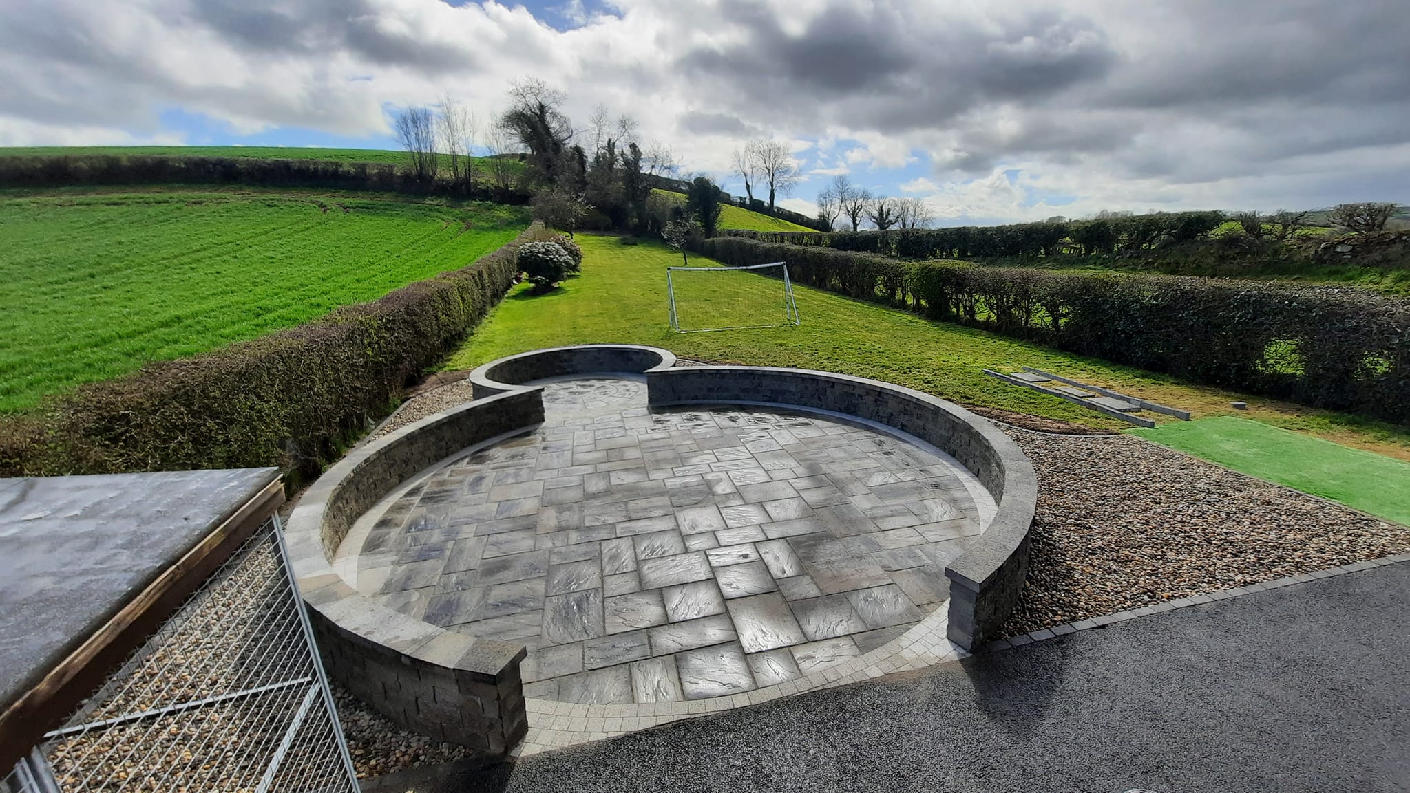 Circular paved patio surrounded by stones leading to a grass garden