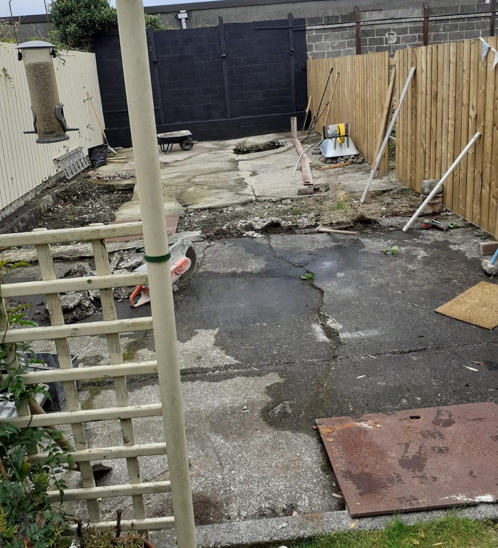 Before picture of a garden with cracked concrete and broken fence